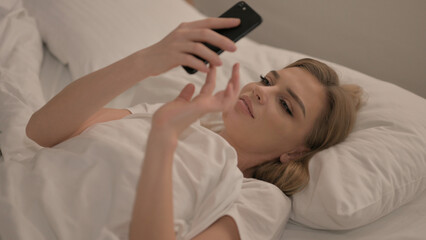 Obraz na płótnie Canvas Young Woman using Smartphone while Lying in Bed