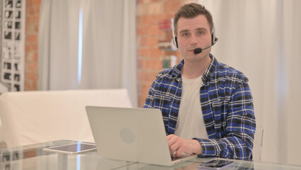 Young Casual Man with Headset Looking toward Camera in Call Center