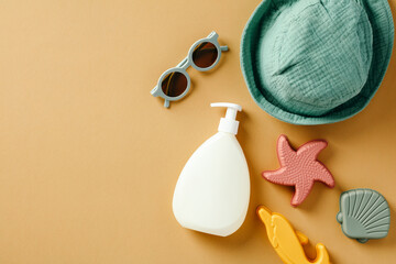 Baby sun lotion, sunglasses, panama, sand toys on sand color background.