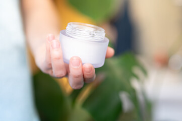  A jar of cream in female hands on blurred abstract background. Young woman holding a face cream in her hands.