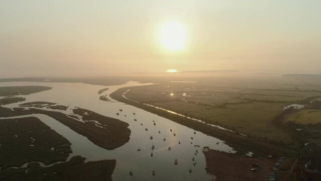 High Establishing Aerial Drone Shot Flying Over Burnham Overy Staithe Coastal Village Creek into the Sun at Sunrise with Small Boats and Fog North Norfolk UK East Coast