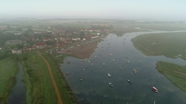 Establishing Aerial Drone Shot Descending on Burnham Overy Staithe Coastal Village on Foggy Morning at High Tide with Boats in North Norfolk UK East Coast