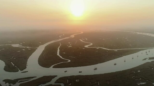 Descending Aerial Drone Shot Towards Salt Marsh and Creek with Sailing Boats into the Sun at Stunning Beautiful Sunrise in Burnham Overy Staithe North Norfolk UK East Coast