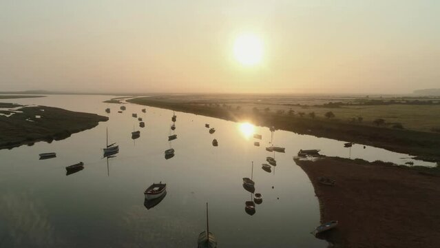 Pullback Aerial Drone Shot of Sailing Boats in Creek at Sunrise into the Sun on Misty Morning at Burnham Overy Staithe North Norfolk UK East Coast