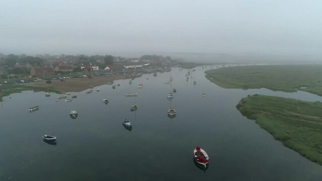 Establishing Moody Aerial Drone Shot Over Creek with Boats Towards Burnham Overy Staithe Coastal Village on Misty Morning in North Norfolk UK East Coast