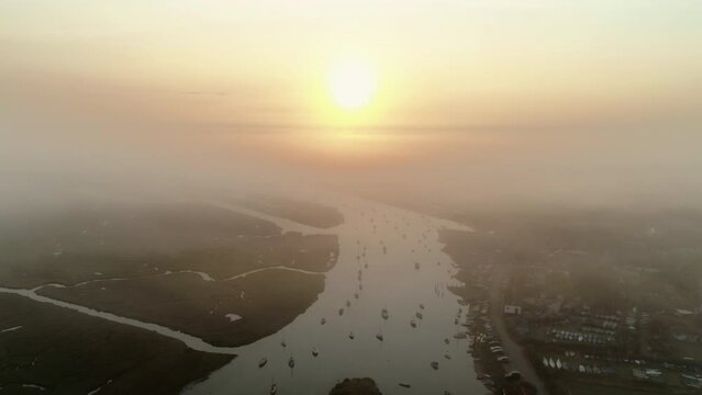 High Pullback Establishing Aerial Drone Shot into the Sun at Stunning Misty Sunrise Over Burnham Overy Staithe Coastal Town and Creek with Boats