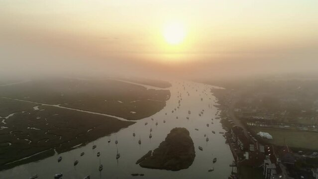 Descending Establishing Aerial Drone Shot From Above Burnham Overy Staithe Coastal Village to the Creek with Boats into the Sun on Stunning Foggy Sunrise in North Norfolk UK East Coast