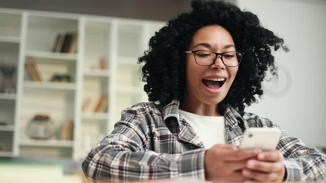 Portrait of overjoyed young african american woman student celebrate online win success reading great news message feel amazed happy on smartphone screen at home Triumph Jackpot Lucky Wow concept