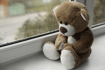 Cute lonely teddy bear on windowsill indoors. Space for text