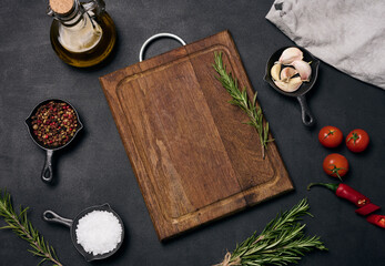 Empty brown wooden board and spices on black table, top view