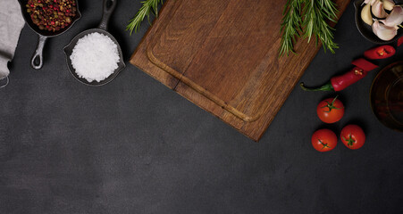 Empty brown wooden board and spices on black table, top view