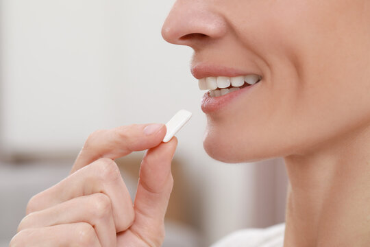 Woman Putting Chewing Gum Into Mouth On Blurred Background, Closeup