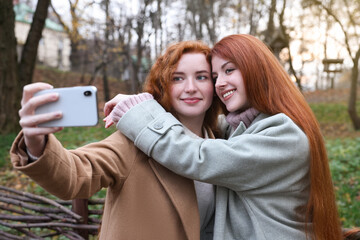 Beautiful young redhead sisters taking selfie in park on autumn day