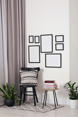 Empty frames hanging on white wall, wooden chair and table with books indoors