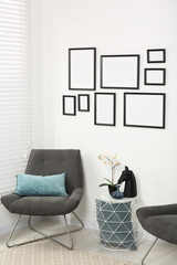 Stylish room interior with empty frames hanging on white wall and comfortable furniture
