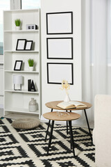 Stylish room interior with empty frames hanging on white wall near shelving unit