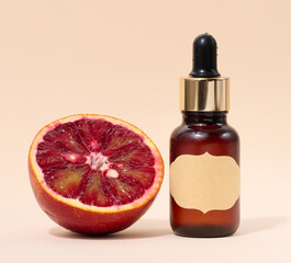 Brown glass bottle with a pipette and a paper label and a half of a red orange on a beige background, oils and cosmetics