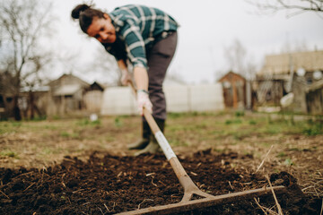 Young woman farmer works with a rake in a field in spring. Preparing the soil before planting. Close-up of a rake in the hands of a woman.