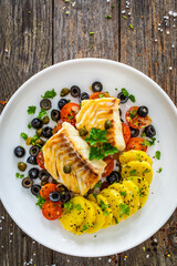 Cod in Italian style on tomatoes and black olives with baked potatoes  on wooden table