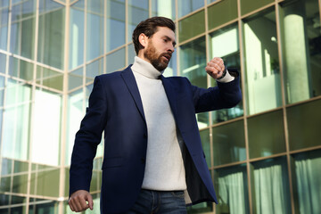 Businessman checking time on watch near building. Being late concept