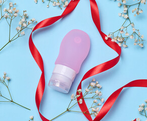 Pink plastic tube for cosmetics and sprigs of white gypsophila flowers, top view