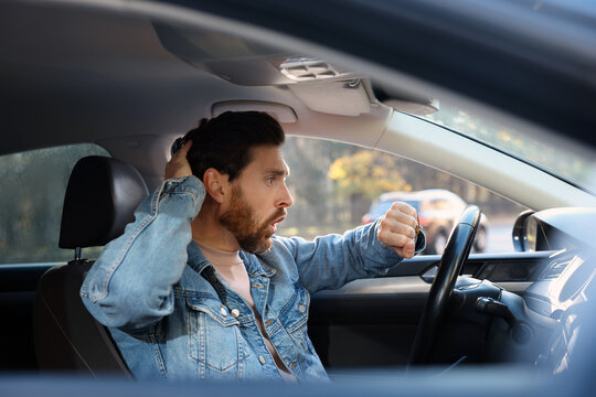 Emotional man checking time on watch in car. Being late concept