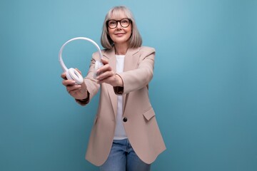 mature 60s business woman listening to music in big headphones on a bright background with copy...