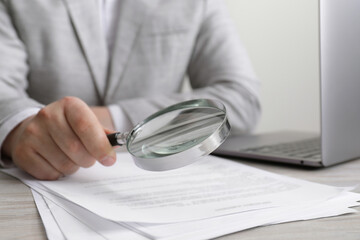Man looking at document through magnifier at white wooden table, closeup. Searching concept
