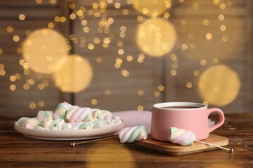 Cup of delicious hot chocolate and marshmallows on wooden table against festive lights