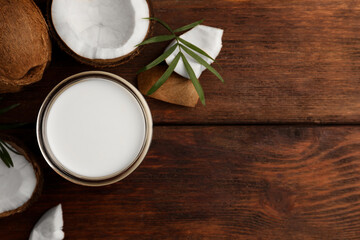 Glass of delicious vegan milk, coconut pieces and palm leaf on wooden table, flat lay. Space for text