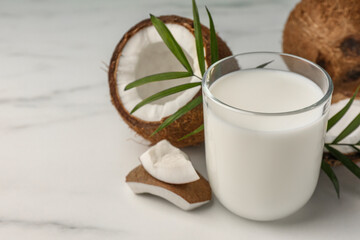 Glass of delicious vegan milk, coconut pieces and palm leaves on white marble table. Space for text