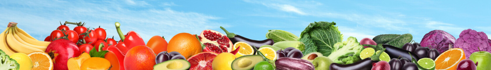 Many different fresh fruits and vegetables against blue sky with clouds. Banner design