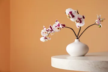 Gordijnen Vase with orchid flowers on white table near light brown wall. Space for text © New Africa