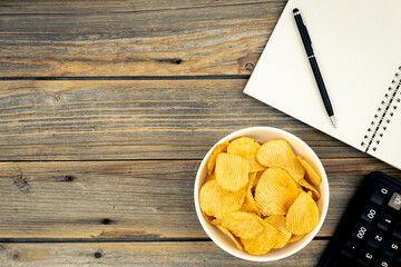 A plate of potato chips, a calculator and a notebook, top view.