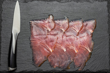 Kitchen knife and thin slices of tuna on stone board.
