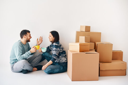 Happy carefree couple talking sitting on floor at their new apartment in moving day.