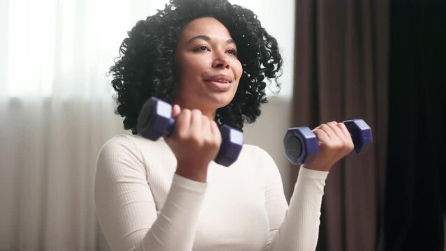 Portrait of charming african american woman working out dumbbell biceps exercise at home Athletic fit strong curly woman do fitness for healthy body indoors
