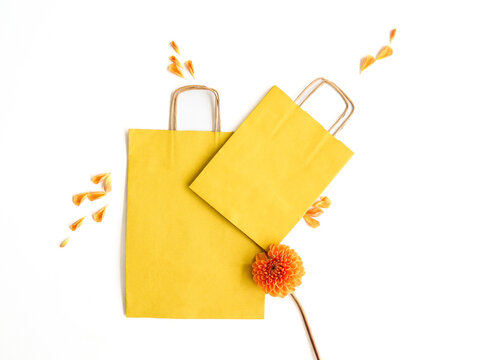 Yellow craft bags with an orange flower on a white background. Spring and summer decor for a gift, holiday, own brand, image. Place for text and logo. Packaging concept.