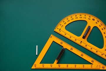Protractor, triangle and chalk on green chalkboard, flat lay. Space for text
