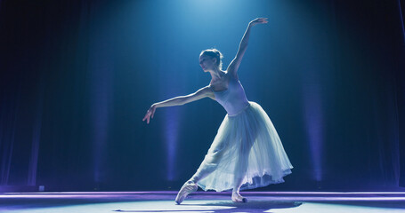 Cinematic Shot of Ballerina in Pointe Shoes and White Tutu Dancing and Rehearsing on Classic Theatre Stage with Dramatic Lighting. Graceful Classical Ballet Female Dancer Performing a Choreography