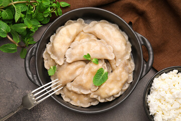 Delicious dumplings (varenyky) with cottage cheese and mint served on brown table, flat lay