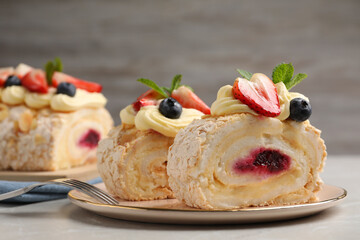 Pieces of tasty meringue roll with jam, cream, strawberry, blueberry and mint on light grey table, closeup