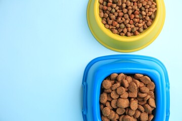 Dry pet food in feeding bowls on light blue background, flat lay. Space for text