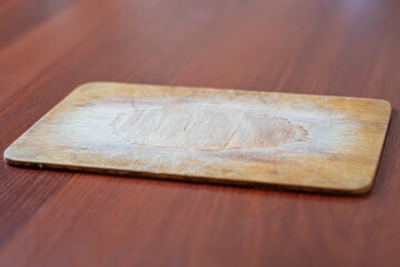 An old wooden board for cutting vegetables with knife scratches. Vintage kitchen appliance for cooking food.