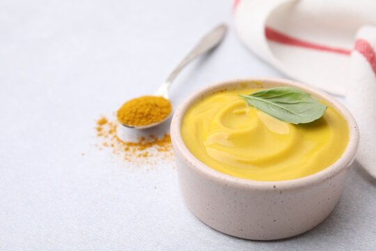 Tasty curry sauce, powder and basil leaf on light table, closeup. Space for text