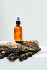 Amber spray bottle with facial treatment on a dry bark on a white background. Front view