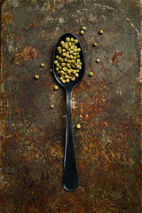 Green pepper peas in a metal spoon. Spices and condiments. Top view. On an old background.