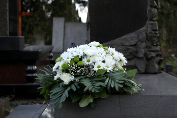 Funeral wreath of flowers on granite tombstone in cemetery