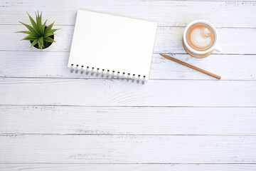 Blank notepad and coffee cup with green plant on modern white table desk background ,Top view with copy space