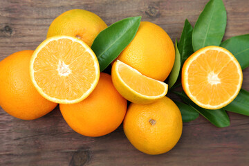 Many ripe oranges and green leaves on wooden table, flat lay